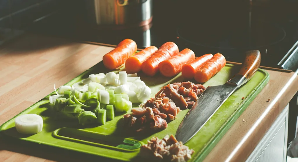 Carrots, chopped leeks and diced meat laid out on a cutting board next to a knife, ready for cooking